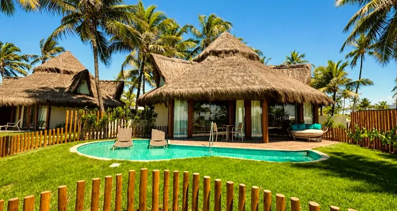 Bangalô Summerville com telhado de palha, piscina privativa e gramado cercado entre coqueiros