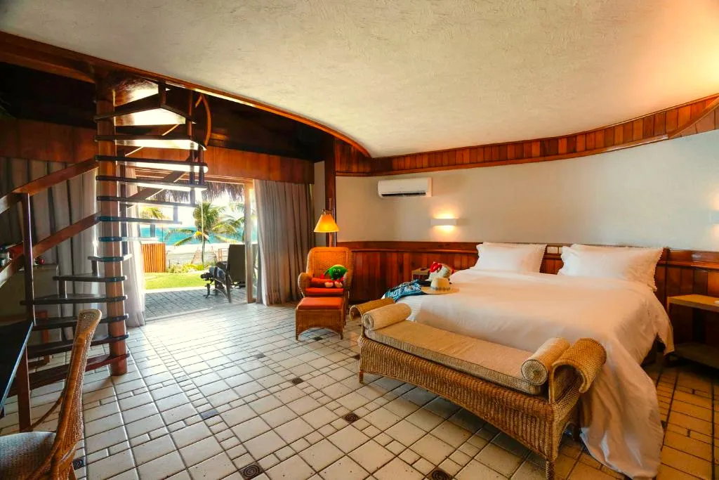 Quarto do térreo do bangalô com cama king, escada caracol e porta para a varanda