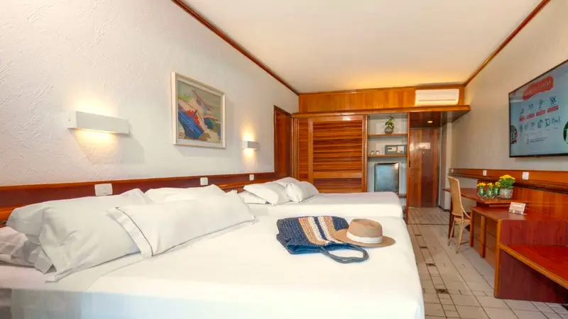 Cama do Apartamento Classic com bolsa de praia e chapéu sobre o lençol branco