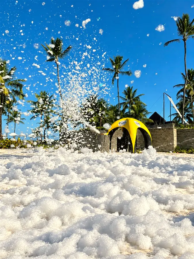 Festa da espuma no gramado, com espuma no ar e coqueiros ao fundo