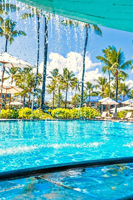 Piscina vista através de gotas d’água, com coqueiros e guarda-sóis