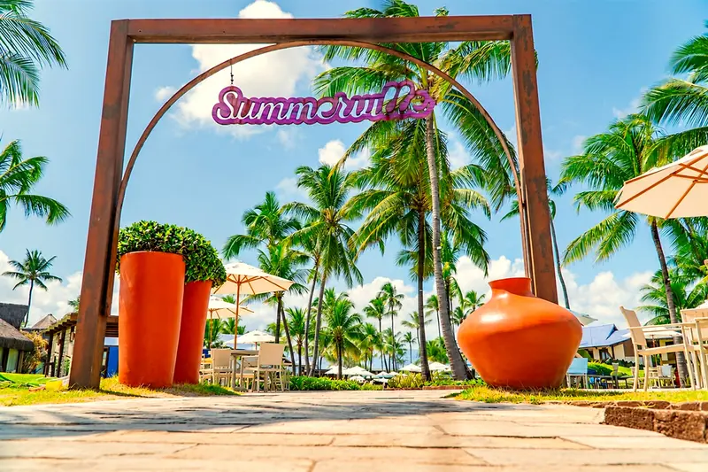 Portal de madeira com o letreiro Summerville, vasos laranja e coqueiros