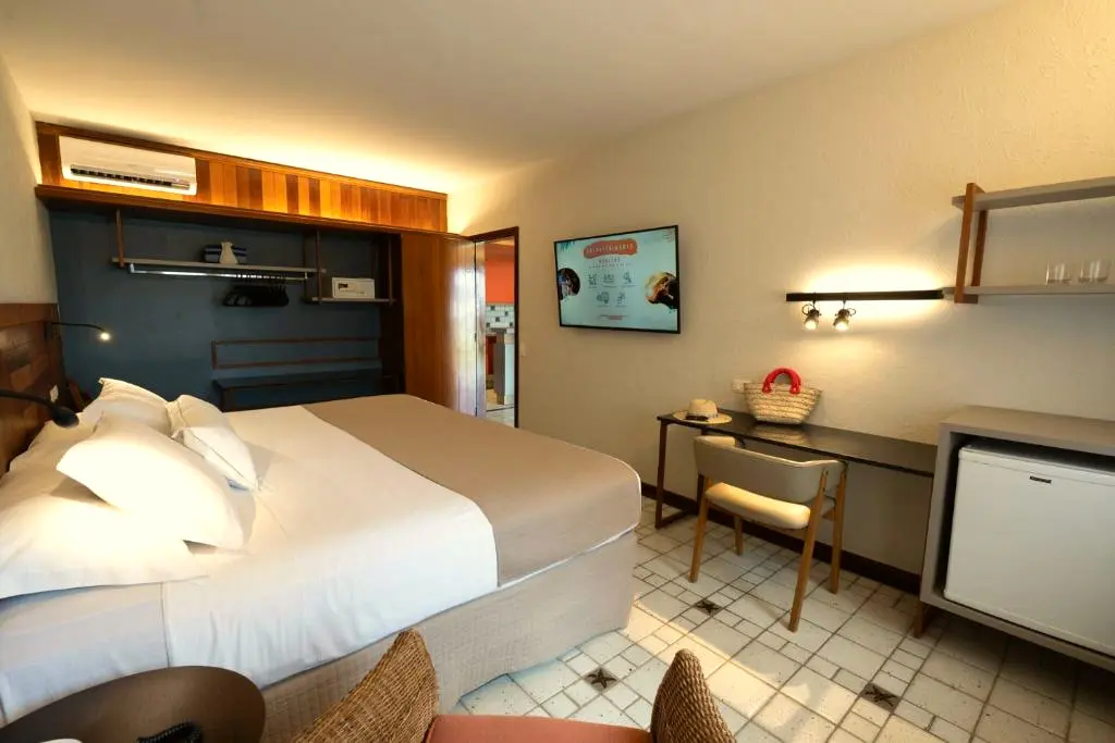 Quarto com cama de casal, mesa de trabalho, frigobar e TV na parede