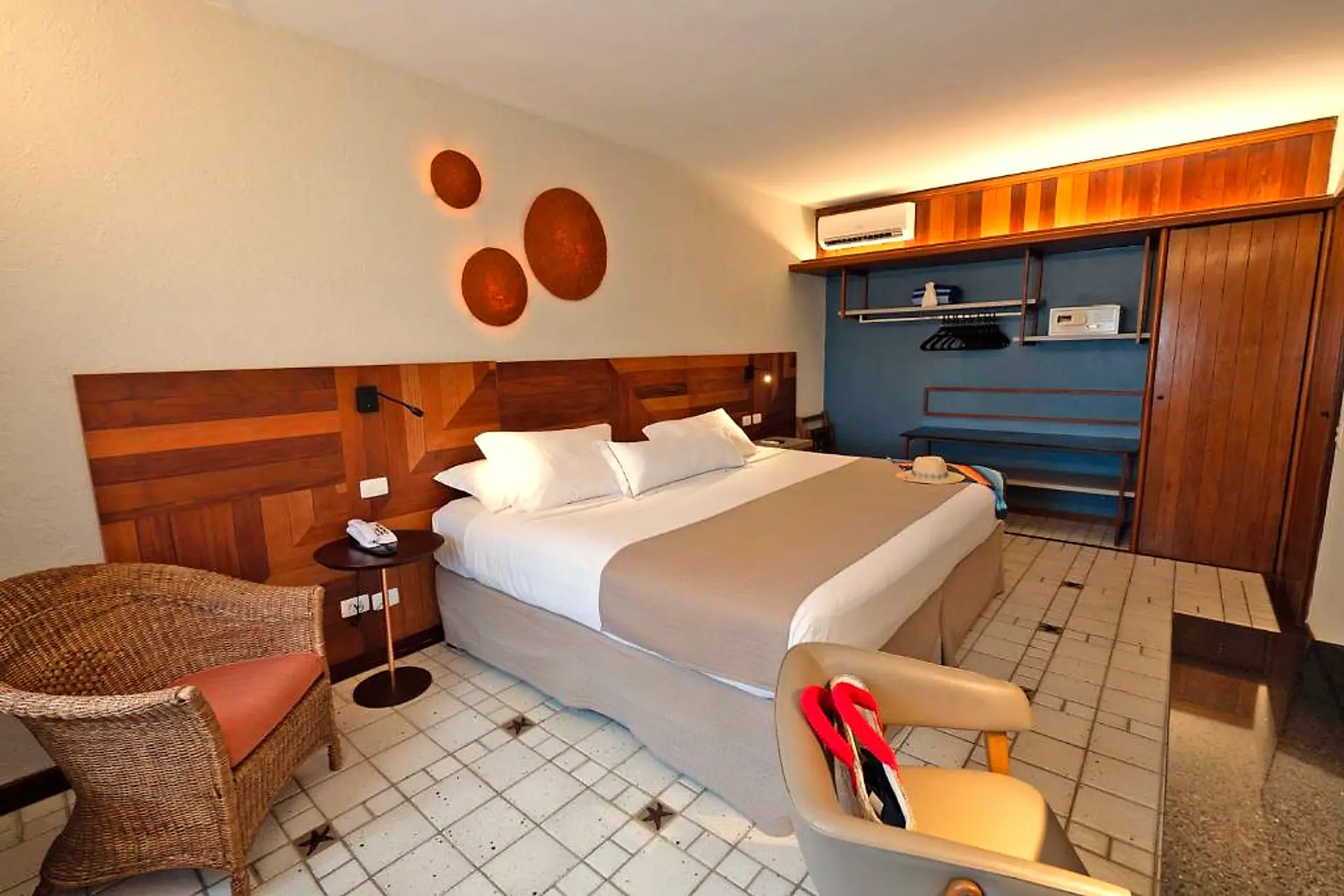Quarto do casal com cama de casal, poltrona de vime e armário aberto